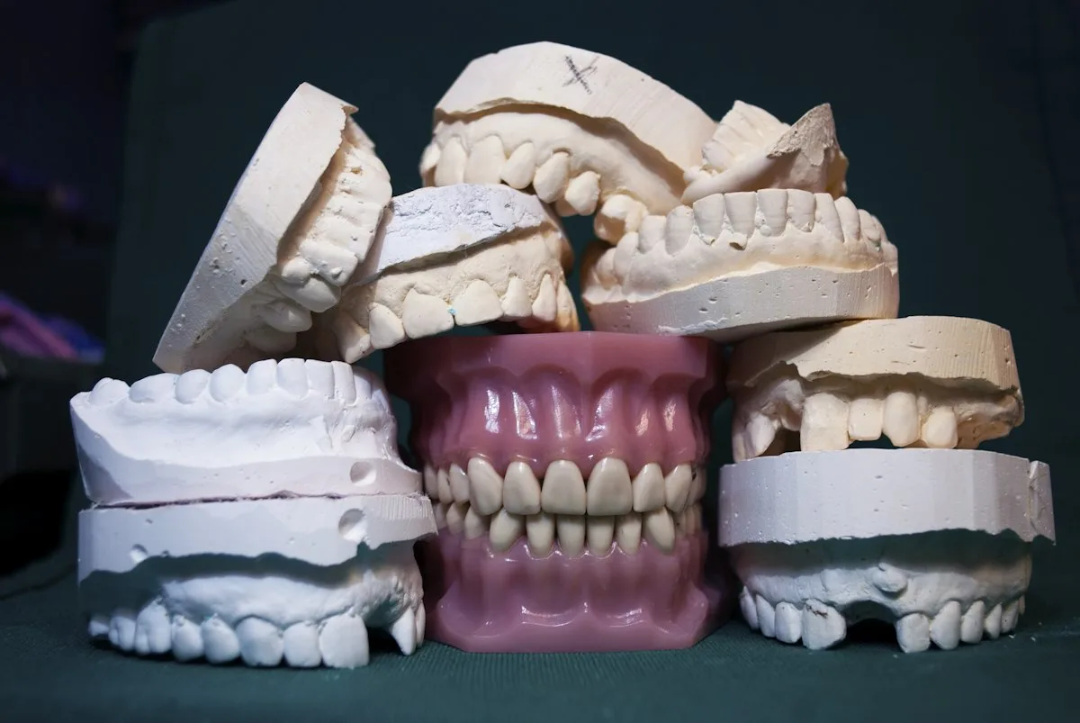 Stone dental models stacked around a complete denture on a dark background